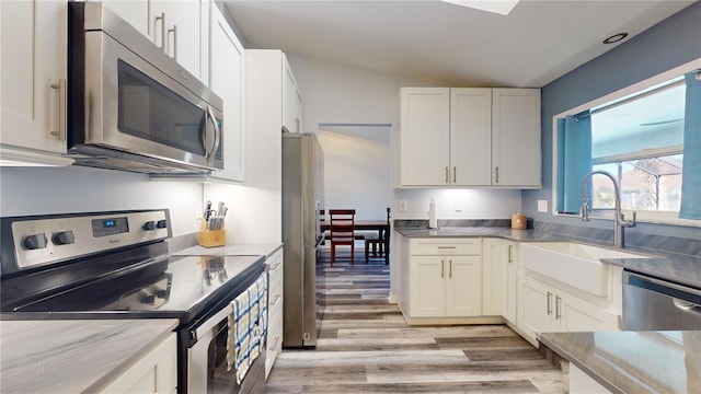 kitchen with stainless steel appliances, white cabinetry, sink, and light hardwood / wood-style flooring