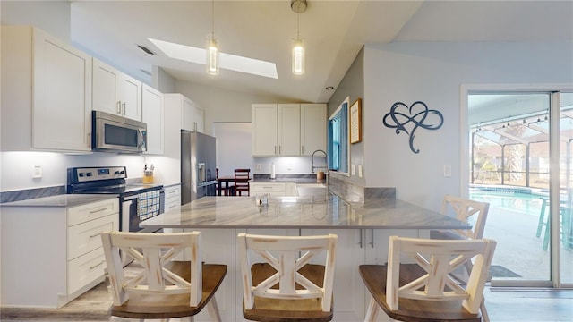 kitchen featuring a kitchen bar, white cabinetry, hanging light fixtures, appliances with stainless steel finishes, and kitchen peninsula