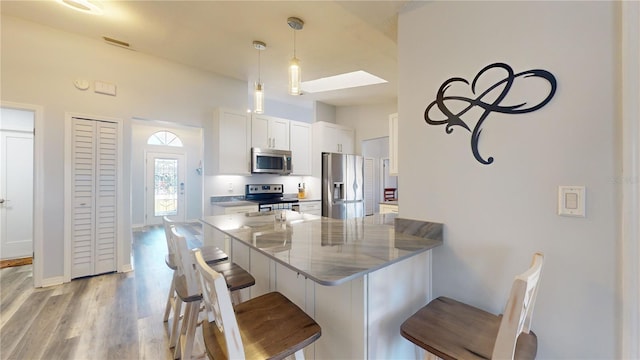 kitchen featuring a breakfast bar area, hanging light fixtures, appliances with stainless steel finishes, kitchen peninsula, and white cabinets