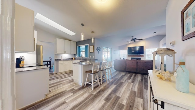 kitchen with pendant lighting, lofted ceiling with skylight, a kitchen breakfast bar, and white cabinets