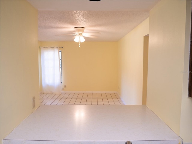 tiled empty room with ceiling fan and a textured ceiling