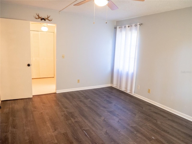 empty room featuring ceiling fan, baseboards, and dark wood finished floors