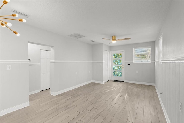 unfurnished room with ceiling fan with notable chandelier, a textured ceiling, and light wood-type flooring