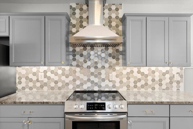 kitchen featuring stainless steel electric stove, tasteful backsplash, gray cabinetry, light stone counters, and wall chimney range hood