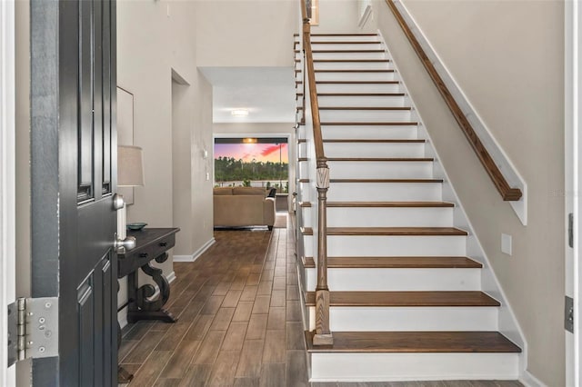 stairway with wood finished floors, baseboards, and a towering ceiling