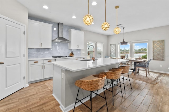 kitchen with a sink, wall chimney range hood, backsplash, light wood-style floors, and light countertops