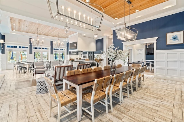 dining space featuring wood ceiling, a high ceiling, a notable chandelier, a decorative wall, and a raised ceiling