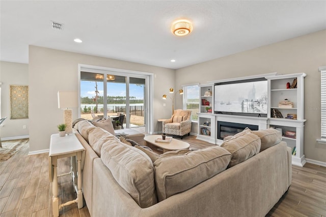 living area with baseboards, visible vents, light wood finished floors, recessed lighting, and a glass covered fireplace