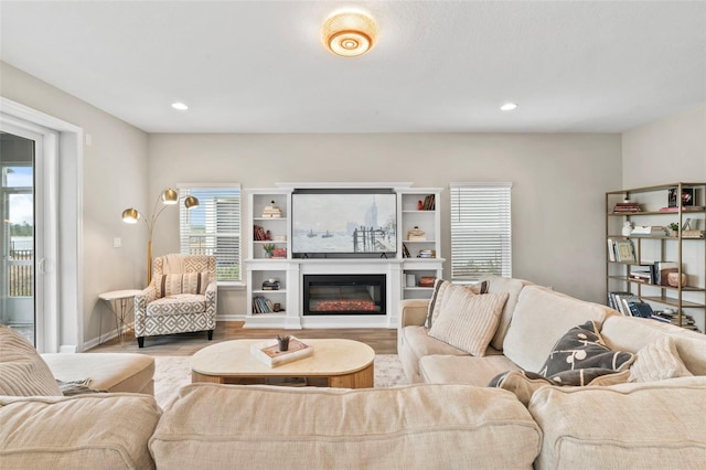 living area with a glass covered fireplace, recessed lighting, and wood finished floors