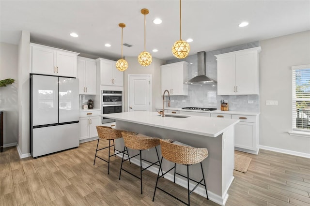 kitchen with visible vents, a sink, stainless steel double oven, white fridge, and wall chimney range hood