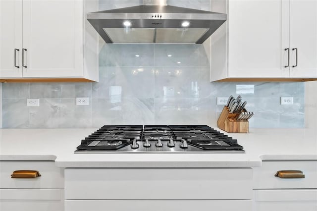 kitchen featuring decorative backsplash, stainless steel gas stovetop, white cabinets, and wall chimney range hood