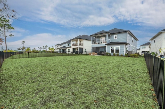 rear view of property featuring a fenced backyard, a balcony, and a yard