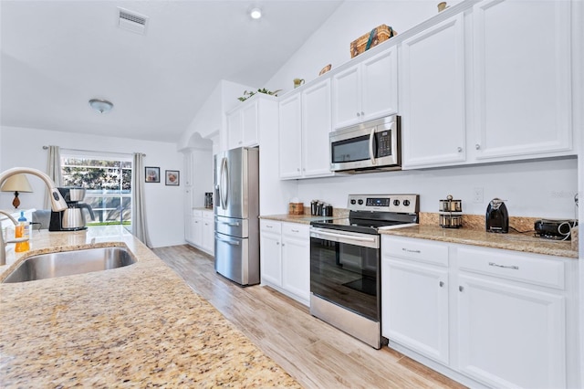 kitchen with lofted ceiling, sink, white cabinetry, light hardwood / wood-style flooring, and stainless steel appliances