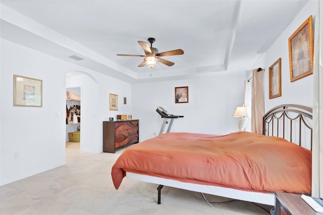 bedroom featuring a spacious closet, a raised ceiling, and ceiling fan