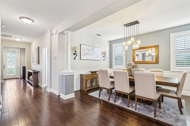 dining space with visible vents, baseboards, dark wood finished floors, a textured ceiling, and ornate columns