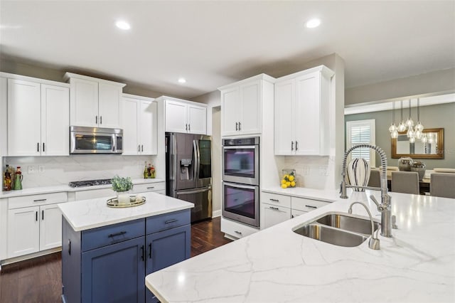 kitchen with sink, light stone counters, pendant lighting, stainless steel appliances, and white cabinets