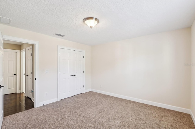 unfurnished bedroom featuring baseboards, visible vents, dark carpet, and a textured ceiling