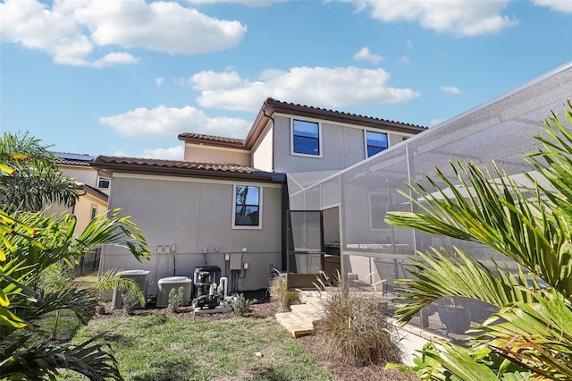 rear view of property with stucco siding, cooling unit, glass enclosure, and a tiled roof