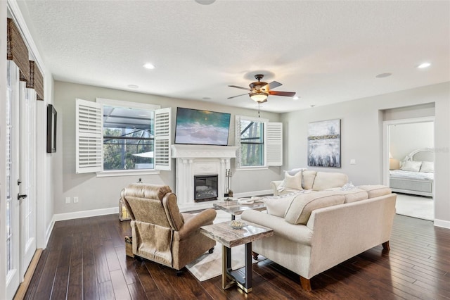 living area featuring a glass covered fireplace, a textured ceiling, dark wood-style floors, and a ceiling fan