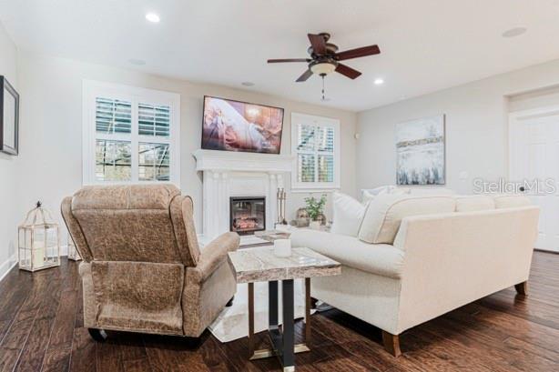 living area with a glass covered fireplace, plenty of natural light, ceiling fan, and dark wood finished floors