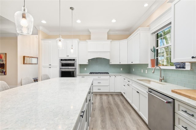 kitchen with white cabinetry, sink, hanging light fixtures, ornamental molding, and stainless steel appliances