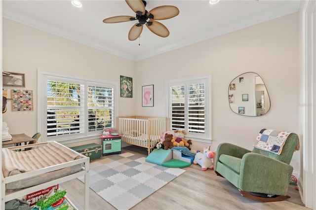 bedroom with crown molding, ceiling fan, a nursery area, and light hardwood / wood-style flooring