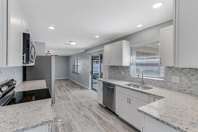 kitchen with sink, white cabinets, backsplash, stainless steel appliances, and light stone countertops