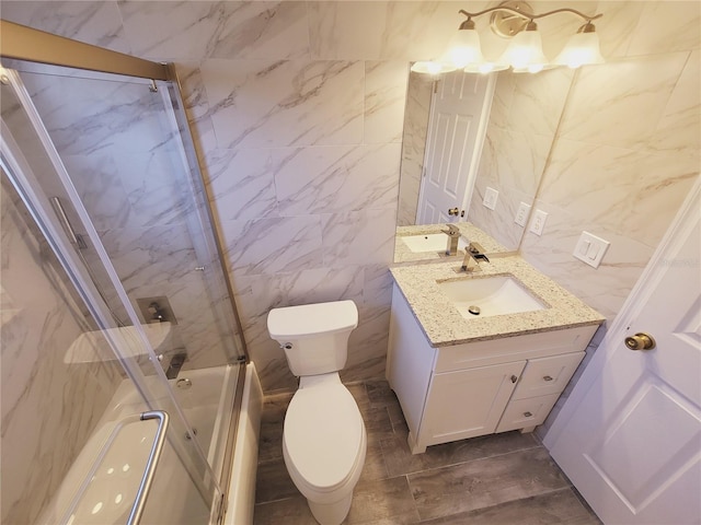 full bathroom featuring vanity, toilet, combined bath / shower with glass door, and tile walls