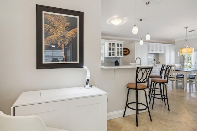 kitchen featuring white cabinetry, a kitchen bar, decorative backsplash, hanging light fixtures, and crown molding