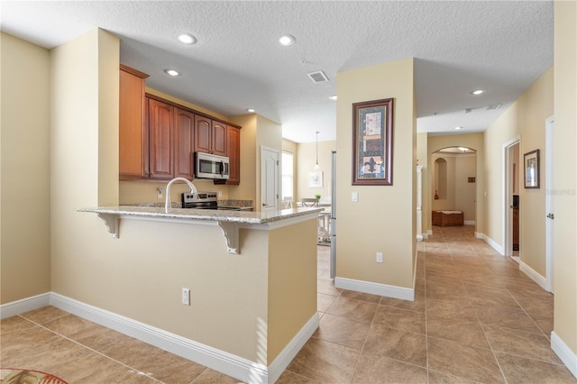 kitchen with a breakfast bar area, stainless steel appliances, light stone counters, a textured ceiling, and kitchen peninsula