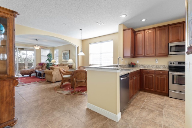 kitchen featuring sink, appliances with stainless steel finishes, hanging light fixtures, light stone counters, and a healthy amount of sunlight