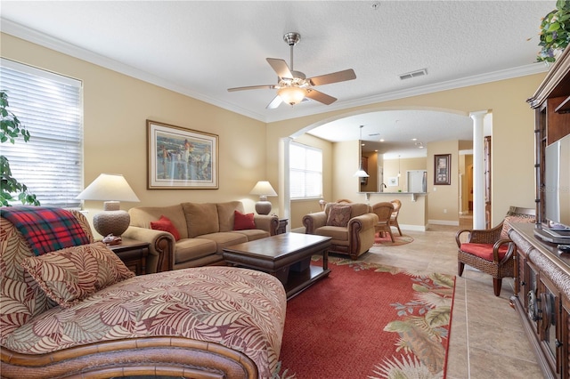 tiled living room featuring ornate columns, crown molding, a textured ceiling, and ceiling fan