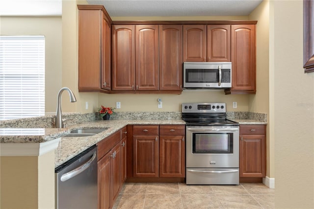 kitchen with sink, light tile patterned floors, stainless steel appliances, light stone counters, and kitchen peninsula