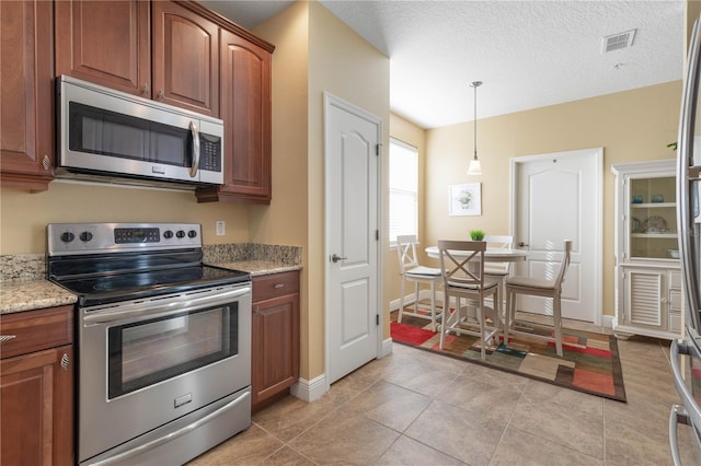 kitchen featuring light tile patterned flooring, decorative light fixtures, a textured ceiling, stainless steel appliances, and light stone countertops