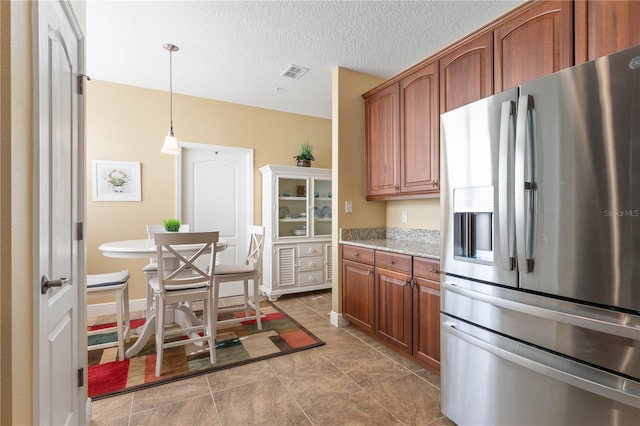 kitchen with pendant lighting, light stone counters, stainless steel fridge with ice dispenser, and a textured ceiling