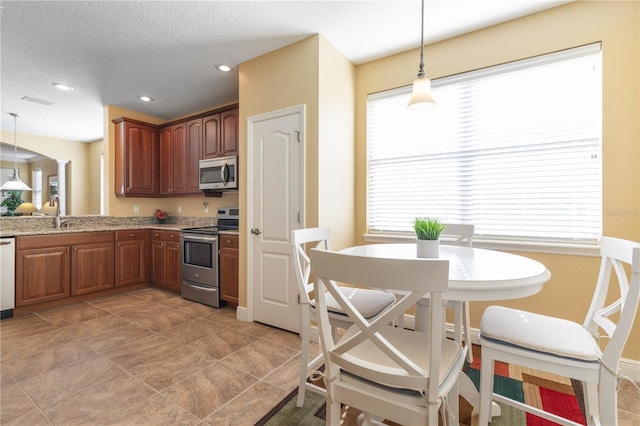 kitchen featuring decorative light fixtures, sink, light stone counters, stainless steel appliances, and a textured ceiling