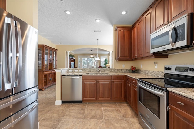 kitchen with sink, light stone counters, kitchen peninsula, pendant lighting, and stainless steel appliances