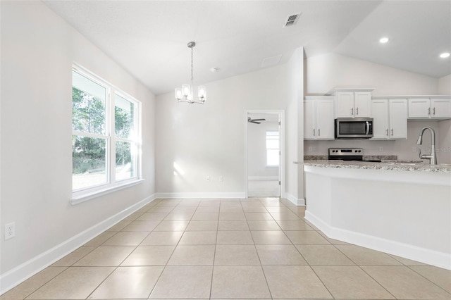 kitchen with pendant lighting, appliances with stainless steel finishes, white cabinetry, light stone counters, and light tile patterned flooring