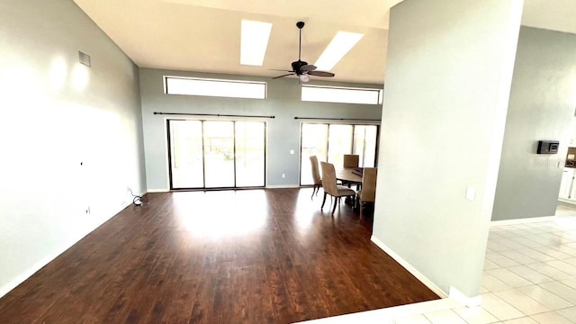 unfurnished living room with a high ceiling, a skylight, ceiling fan, and light hardwood / wood-style floors