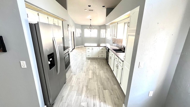 kitchen with sink, appliances with stainless steel finishes, white cabinetry, hanging light fixtures, and a notable chandelier