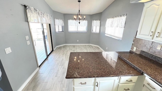 kitchen featuring plenty of natural light, vaulted ceiling, dark stone counters, and white cabinets