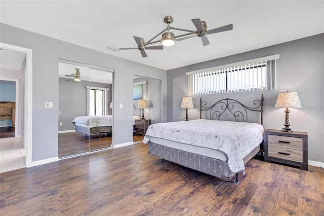 bedroom featuring ceiling fan, dark hardwood / wood-style floors, and two closets