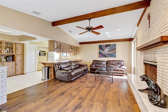 living room featuring vaulted ceiling with beams, a fireplace, ceiling fan, and light wood-type flooring