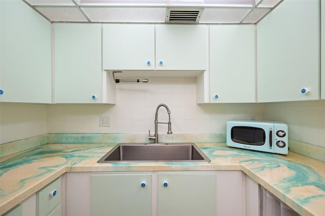 kitchen with tasteful backsplash, white cabinetry, and sink