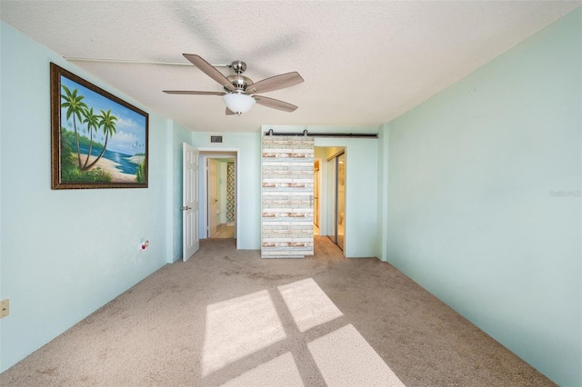 unfurnished bedroom with ceiling fan, a barn door, light carpet, and a textured ceiling