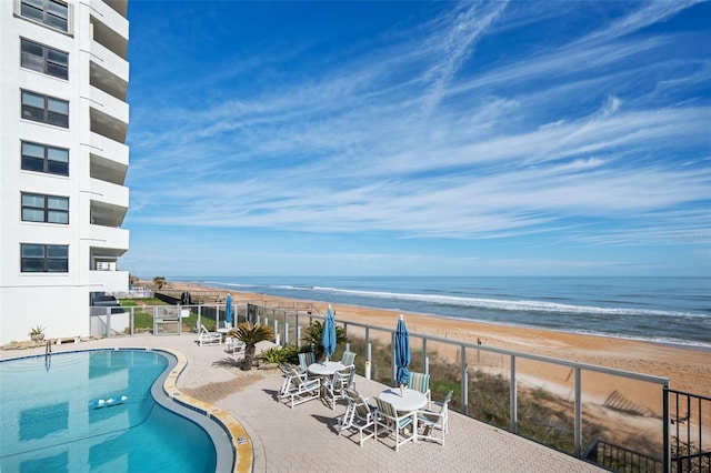 view of swimming pool with a water view, a beach view, and a patio