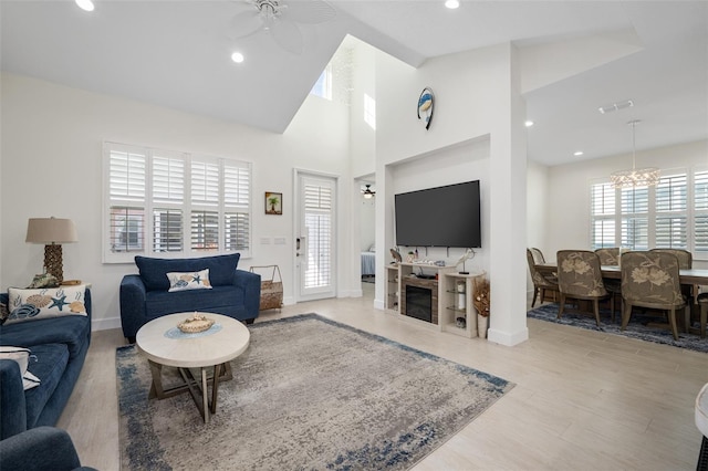 living room featuring high vaulted ceiling, plenty of natural light, ceiling fan with notable chandelier, and light hardwood / wood-style flooring