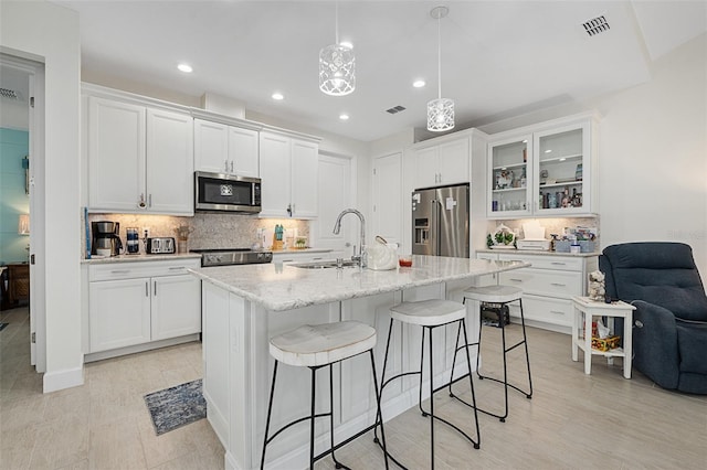 kitchen featuring sink, white cabinetry, hanging light fixtures, stainless steel appliances, and a kitchen island with sink