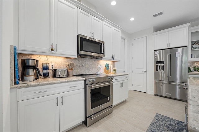 kitchen featuring stainless steel appliances, light stone countertops, decorative backsplash, and white cabinets