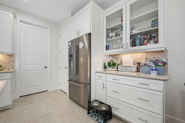 kitchen featuring tasteful backsplash, light stone countertops, high quality fridge, and white cabinets